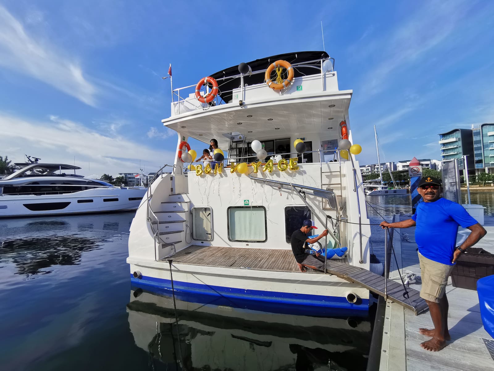 A motor yacht berthed stern-to at the pontoon with balloons along the aft deck, a crew member standing by the lines and another on the boarding platform