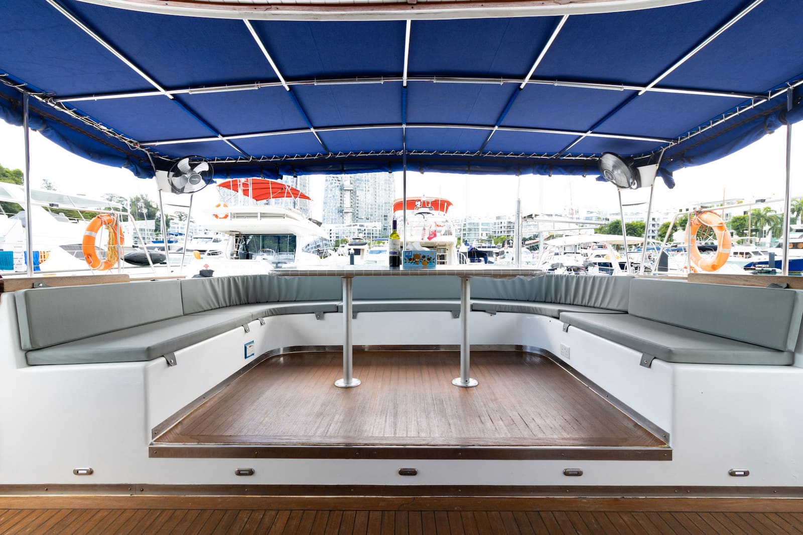 Covered aft deck — wraparound bench seating around the table, mounted fans under the blue awning
