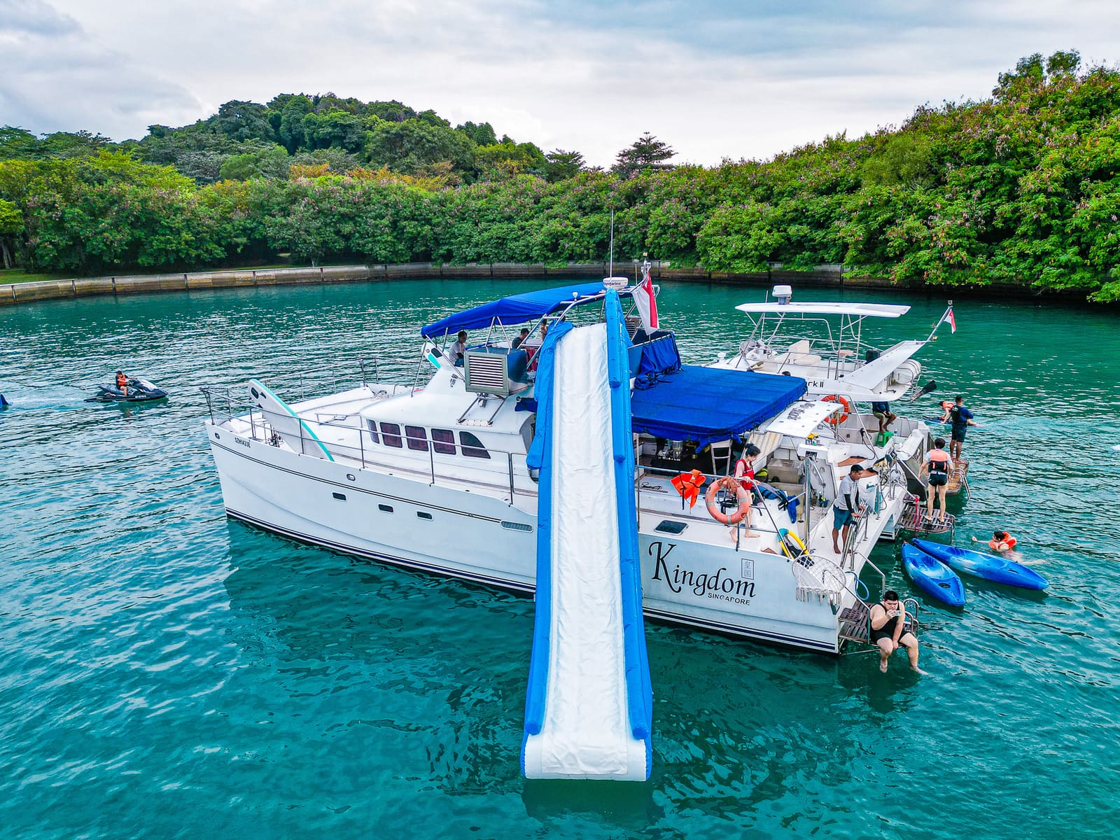 Stern-quarter aerial with the slide and trampoline rigged and swimmers off the stern ladders