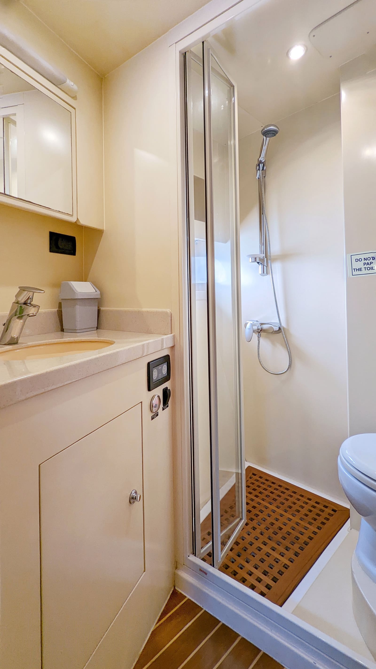 Bathroom with a basin, a separate glass shower cubicle over a teak grating, and a toilet