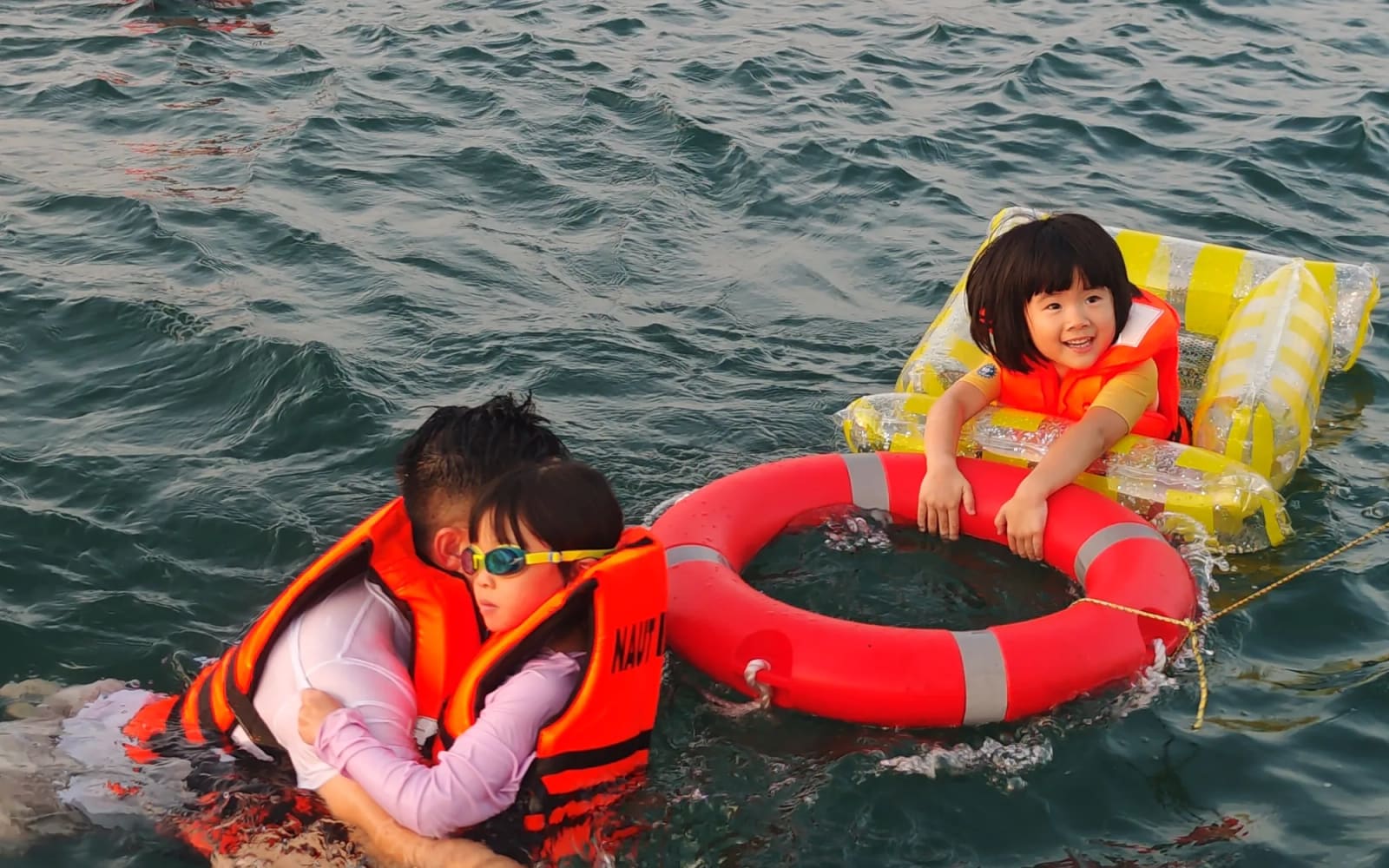 Children in child-size life jackets at the swim stop, holding the lifebuoy off the stern
