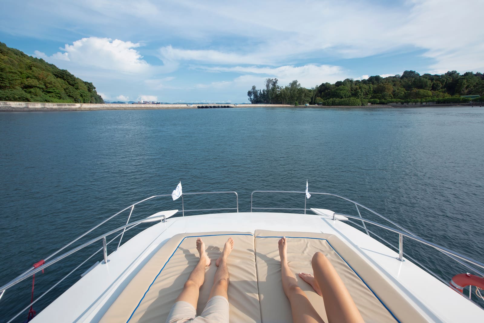 Two guests stretched out on the foredeck sun pads at anchor, looking across to a wooded island