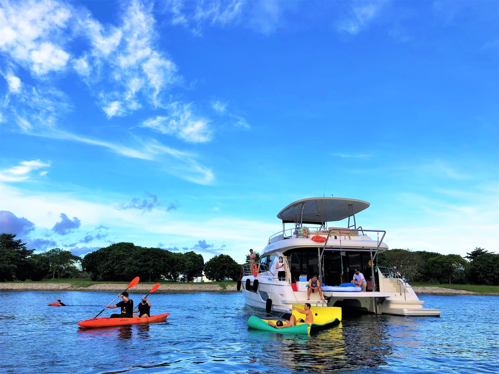 Synergy 1 at anchor with a kayak and the floating mat in the water beside her and guests on the swim platform